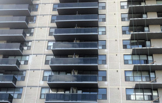 High-rise apartment building with rows of dark balconies and large windows, featuring a modern facade with light-colored brick.