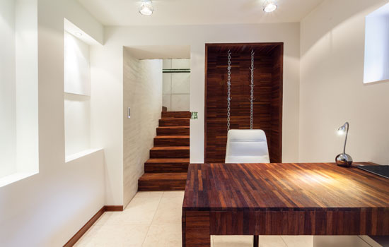 Modern minimalist home office featuring a dark wood desk and matching wood steps leading up to the main floor of a house.