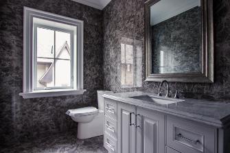 Elegant bathroom with dark marble walls, a large framed mirror, a white vanity with a marble countertop, and a window letting in natural light.