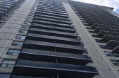 High-rise apartment building with rows of dark balconies and large windows, featuring a modern facade with light-colored brick.