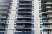High-rise apartment building with rows of dark balconies and large windows, featuring a modern facade with light-colored brick.