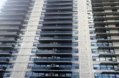High-rise apartment building with rows of dark balconies and large windows, featuring a modern facade with light-colored brick.