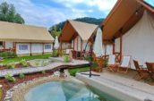 Charming outdoor glamping setup with canvas tents, wooden decks, and a small natural pool.