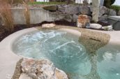 Small outdoor pool with bubbling water, surrounded by natural stone accents and landscaping features, including a rock wall and decorative plants.
