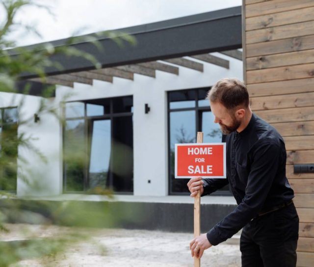 a man holding a home for sale sign